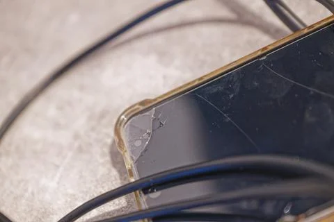 Smartphone with cracked screen and tangled black charging cables on surface Stock Photos
