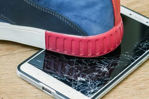 Smartphone display smashed by boot on brown background. Closeup, selective fo Stock Photos