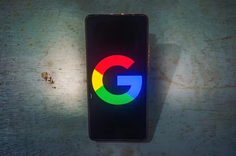 A smartphone displaying the Google logo on its screen, placed on a rustic w.. Stock Photos