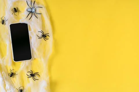 A smartphone with an empty black screen on a yellow background, a spider web. Stock Photos