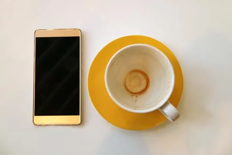 Smartphone with empty cup of finished drinking coffee isolated on white table Photos