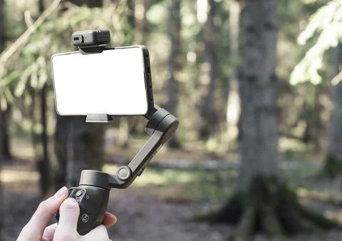 Smartphone on a gimbal in a forest. Handheld stabilizer for mobile filming an Stock Photos