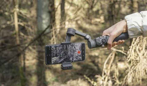 Smartphone on a gimbal stabilizer in a forest. Handheld mobile filming gear f Stock Photos