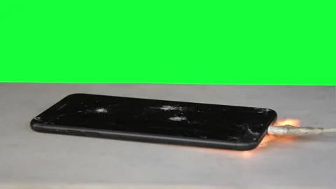 Smartphone on green background ignites from overheating battery, sparks and smok Stockbeeldmateriaal 261519597