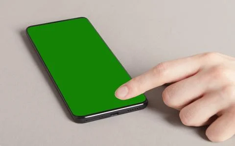 Smartphone with green screen on beige surface. A hand taps the display in clo Stockfoto's