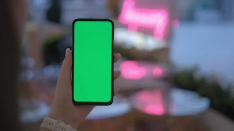 A smartphone with a green screen is being held in a hand against an outdoor Stock Footage 277216164