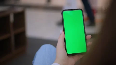 A smartphone with a green screen is being held in a hand against an outdoor Stock-Footage 277409240