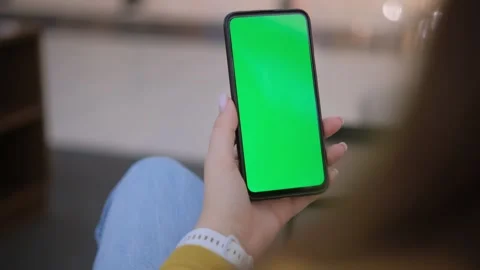 A smartphone with a green screen is being held in a hand against an outdoor Stock-Footage 277848208