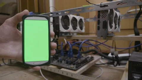 Smartphone with green screen display next to cryptocurrency mining rig held b Stock Footage 102473416