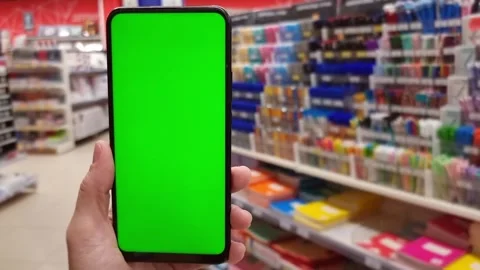 Smartphone with green screen in hand on the background of racks with pens and Stock Footage 281591145