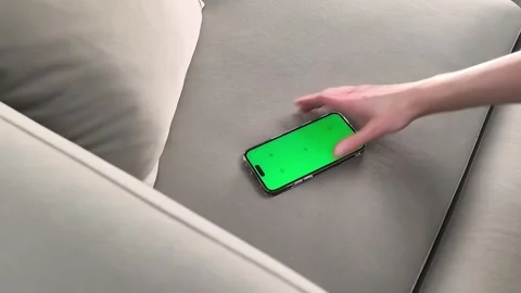 Smartphone with green screen lies on sofa in horizontal position and hand p.. Stock Footage 339854818