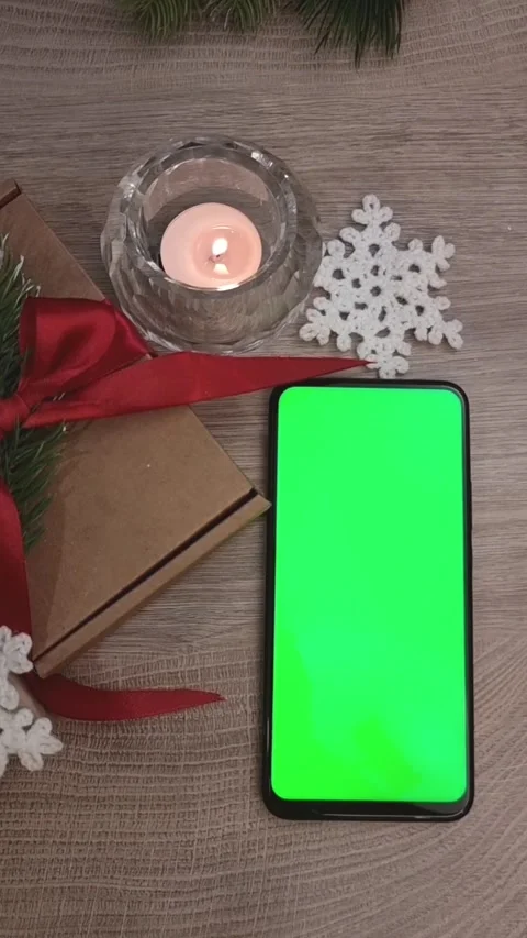 A smartphone with a green screen lies vertically on a wooden table next to a Stock Footage 309403197