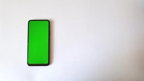 A smartphone with a green screen is lying on a white background, a woman's hand Stock Footage 289014621