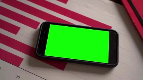 Smartphone with green screen placed on desk with financial charts Stock Footage 265149747