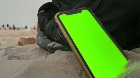 Smartphone green screen vertical on sand. Blurred tourists relaxing on beach Stock Footage 180601406