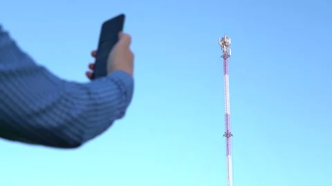 Smartphone in hand against the background of the telecommunication tower Stock Footage 156485162
