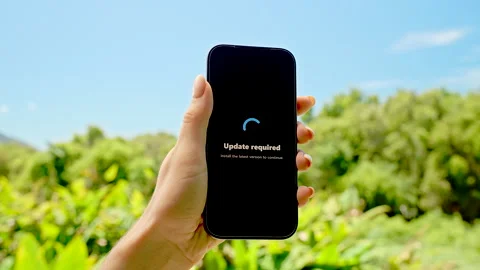 Smartphone in Hand Displaying Update Required Screen Against Sunny Sky and Green Stock Footage 318474717