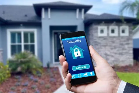 Smartphone with home security app in a hand on the building background. Stock Photos