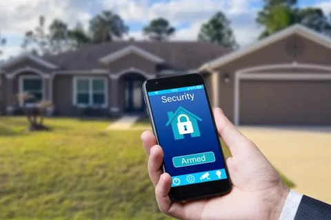 Smartphone with home security app in a hand on the building background. Stock Photos