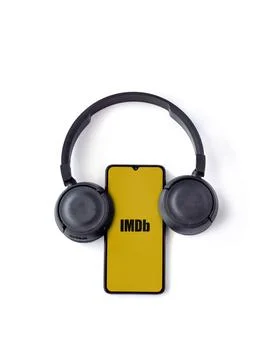 Smartphone with IDMb app launch screen and wireless headphones on white bac.. Stock Photos