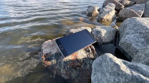 Smartphone Lying on Shoreline Rocks Dangerously Close to Water Stock Footage 340280584