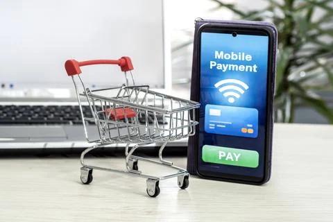 Smartphone with a mobile payment app and shopping cart against a laptop Fotos de archivo