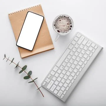 Smartphone mock up with note keyboard coffee cup green plant on white work space Foto stock