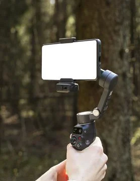 Smartphone mounted on a gimbal stabilizer in a forest. Handheld mobile filmin Stock Photos