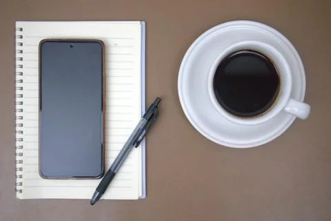 Smartphone, notebook and cup of coffee on brown table Stock Photos