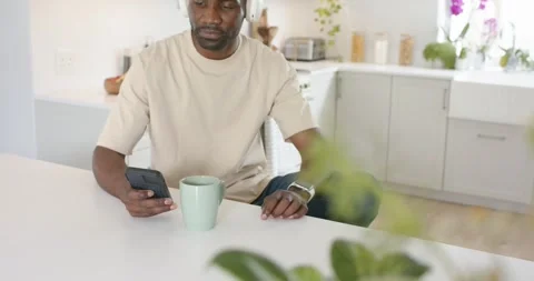 Smartphone pinging, man checking it at counter, putting on headphones, smiling Stock Footage 337160385