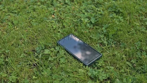 A smartphone is placed on the grass with the screen facing up, lose phone Vídeos de archivo 344526412