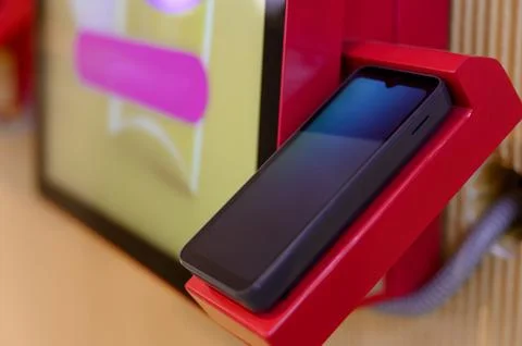 Smartphone placed on red charging dock with digital display in background Stock Photos