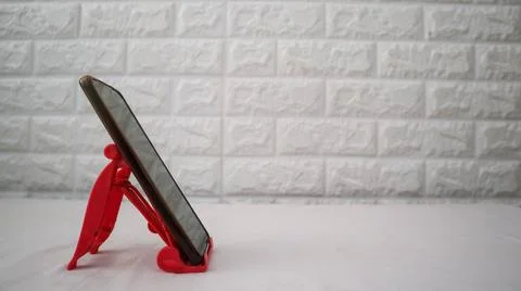 Smartphone placed on a red plastic stand against a textured wall, offering .. Stock Photos