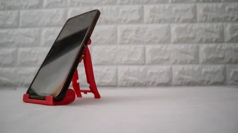 Smartphone placed on a red plastic stand against a textured wall, offering .. Foto stock