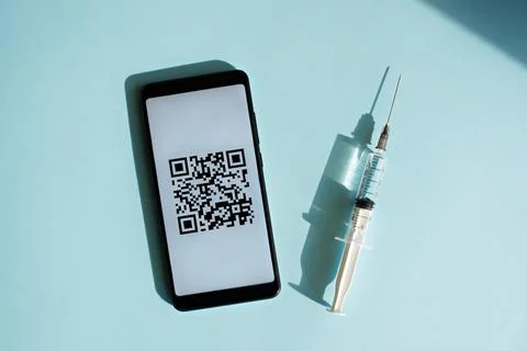 Smartphone with quar code of vaccination certificate on the screen, syringe and Photos