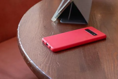 Smartphone in red protective case resting on wooden table beside a tablet s.. Stock Photos
