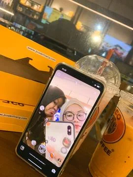 A smartphone rests on an orange cafe table displaying a video call selfie o.. Stock Photos