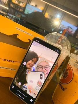 A smartphone rests on an orange cafe table displaying a video call selfie o.. Stock Photos