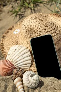 Smartphone on sand with shells and beach hat. Stock Photos