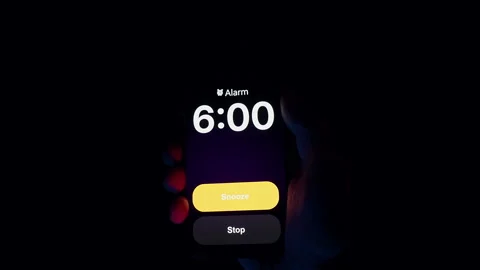 Smartphone Screen Displays Alarm Set for 6 AM Held in Hand Under Blue and Red Stock Footage 319886964
