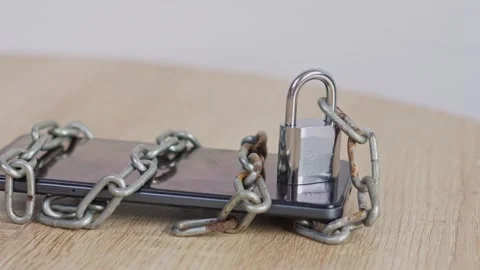 Smartphone secured with metal padlock and rusty chains on wooden surface Stock Footage 328553316