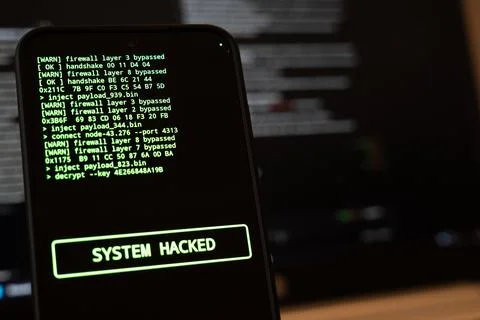 Smartphone showing green hacker code lines and a System Hacked banner on a black Фото
