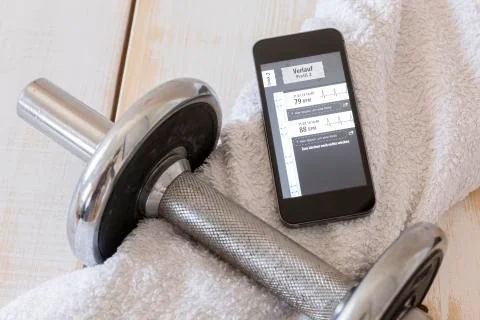 Smartphone showing heart rate monitor, towel, tablets and dumbell on wood Stock Photos