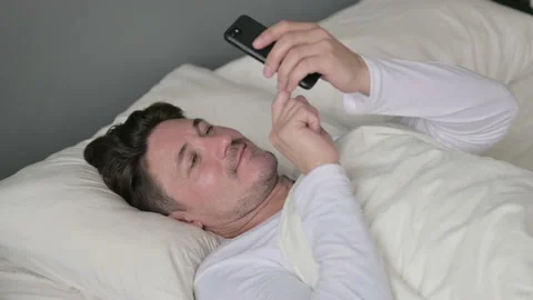 Smartphone use by Middle Aged Man Laying in Bed Video stock 142367606