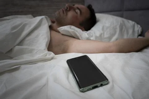 Smartphone User Holding Cellphone While He Sleeps. . Young man snoozing on .. Stockfoto's