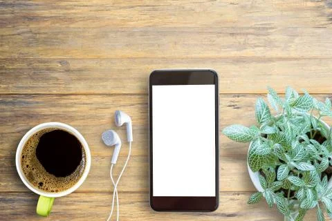 Smartphone white screen, white ear phone and cup of coffee on wooden table ba Foto stock
