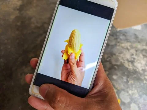 A smartphone whose screen displays an image of a hand holding a banana Foto stock