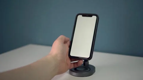 The smartphone is on a wireless charging pad and shows a white screen. The man Stock Footage 314465564