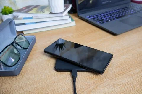 Smartphone on wireless charging pad on working table Stock Photos