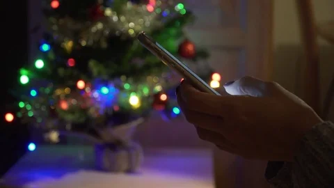 Smartphone in woman's hands. Christmas tree with lights at background. Stock Footage 83997601